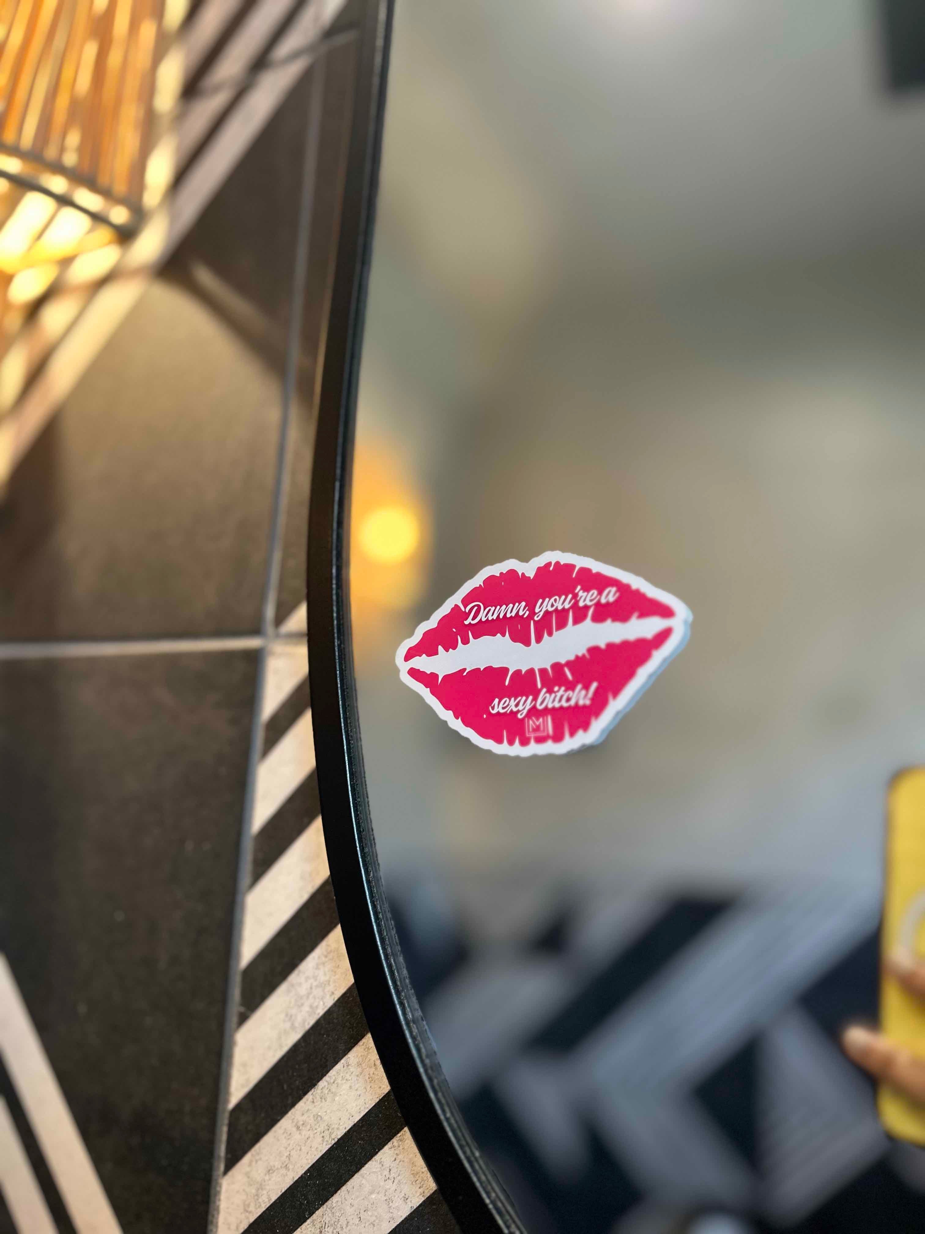 Lipstick kiss sticker with text that reads "Damn, you're a sexy bitch!" on a bathroom mirror