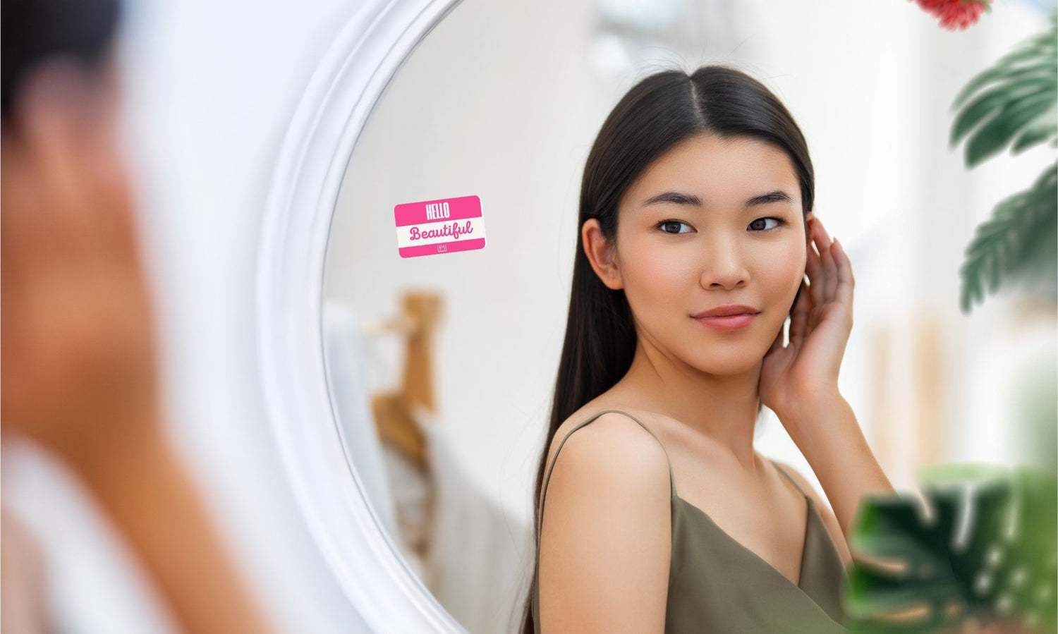 Woman looking at her reflection in the mirror with a blurred background, with a Mirae Mantra vinyl cling on the mirror.