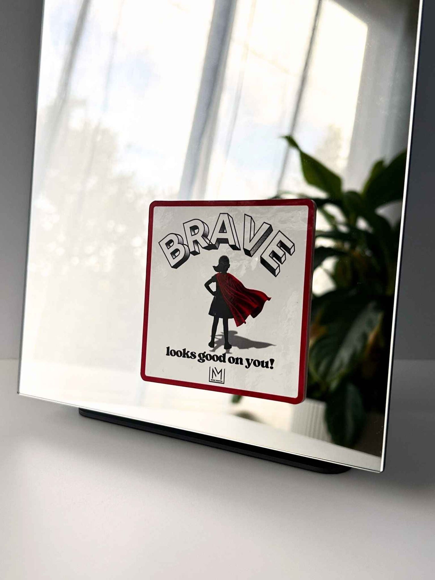 Kids confidence affirmation mirror sticker showing a child in a red cape with the words “Brave looks good on you”