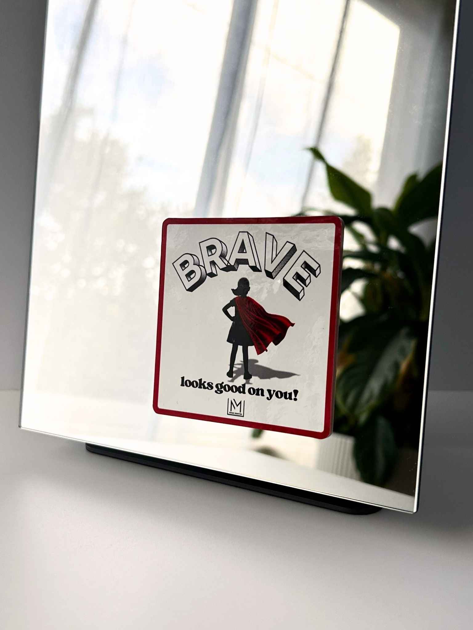 Kids confidence affirmation mirror sticker showing a child in a red cape with the words “Brave looks good on you”