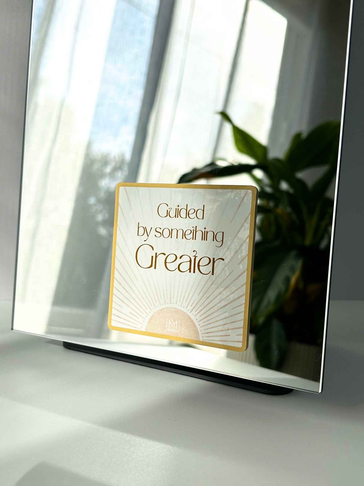 Faith-based mirror affirmation reading “Guided by something greater” with sunburst design