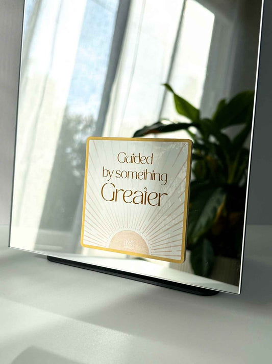 Faith-based mirror affirmation reading “Guided by something greater” with sunburst design