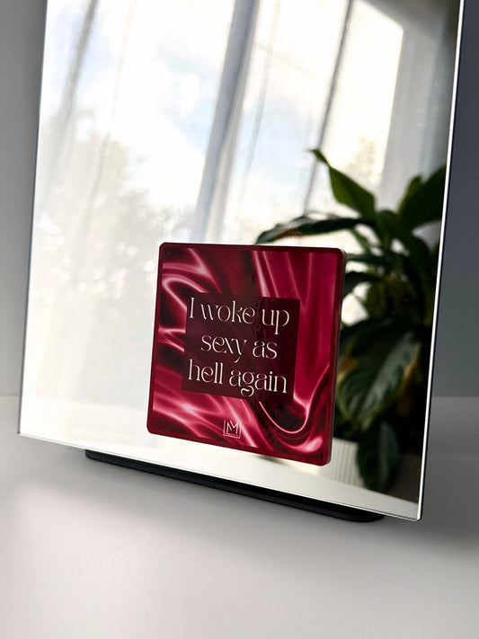 Bold self-love mirror sticker with “I woke up sexy as hell again” text on pink fabric background